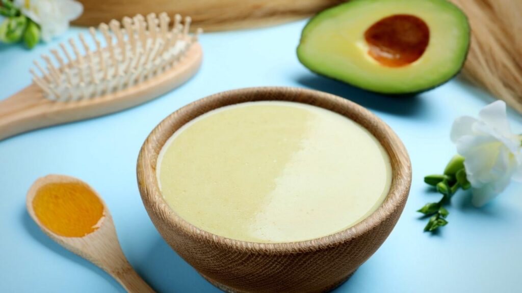 bowl of hair treatment mask, hairbrush, wooden spoon and half avocado