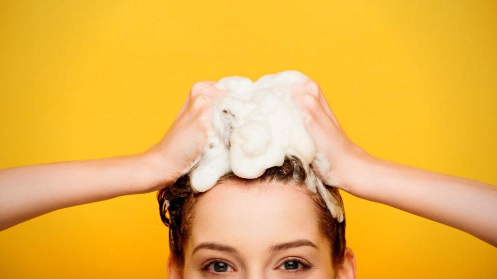 woman with both hands on head lathering hair with shampoo