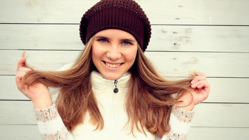  woman in black hat holding ends of her hair up