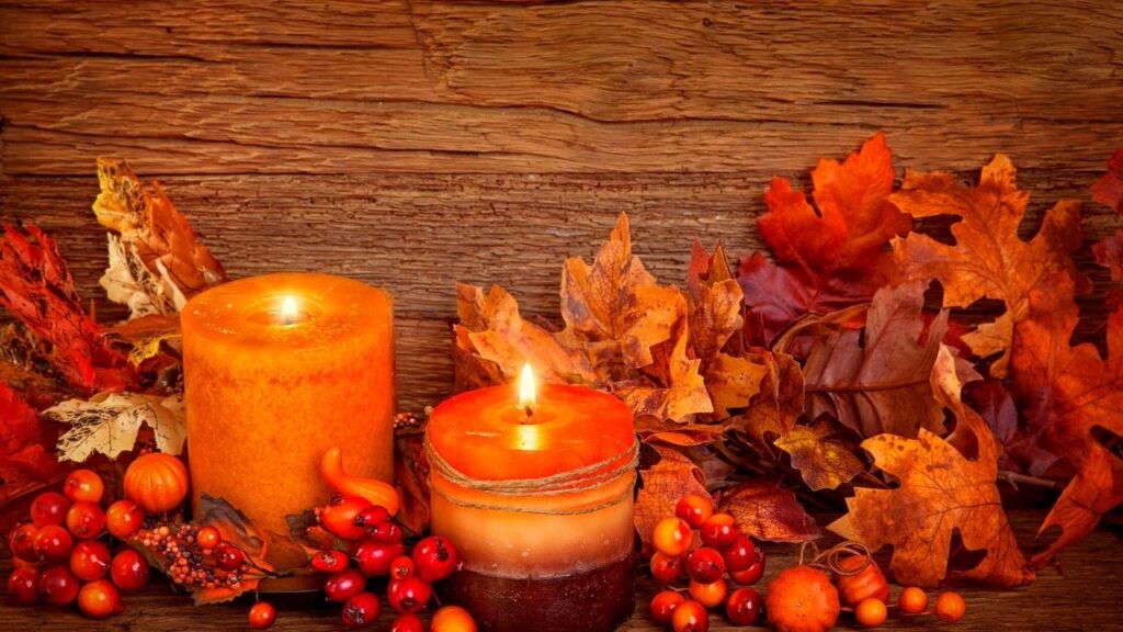 2 lit autumn candles beside leaves and berries