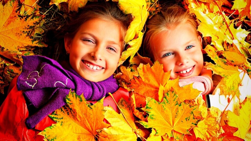 2 happy girls faces above autumn leaves
