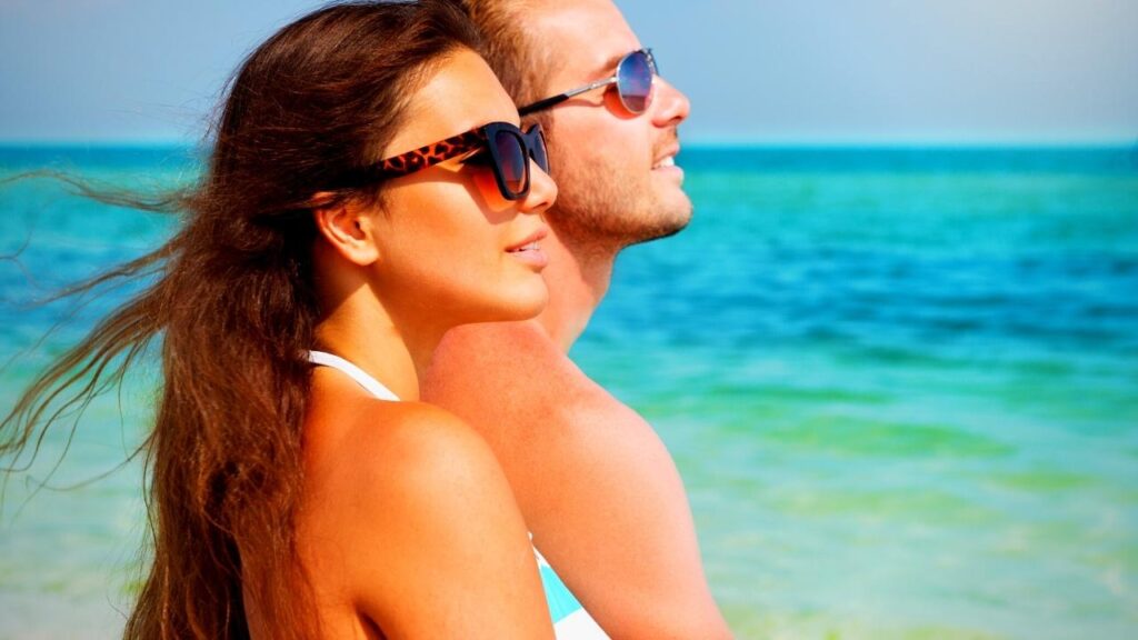 young tanned couple wearing sunglasses on beach