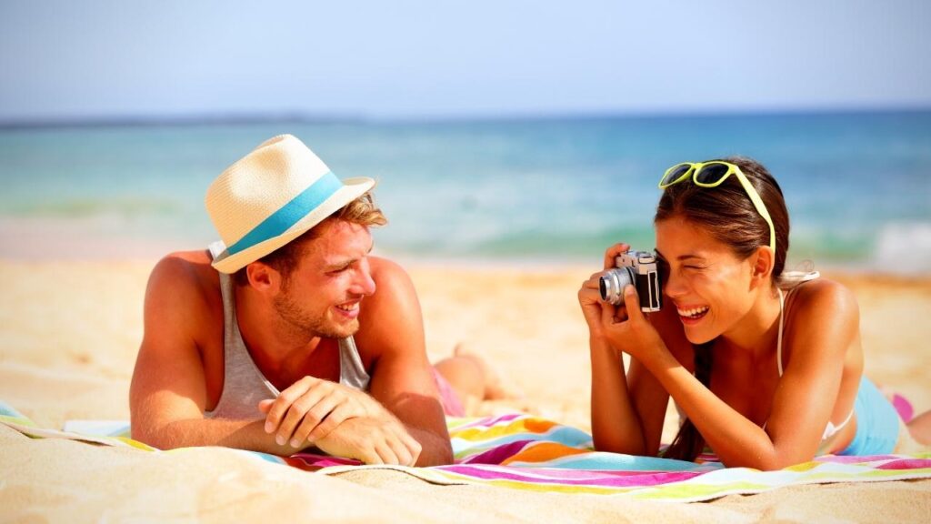 young happy couple with camera enjoying sun on beach