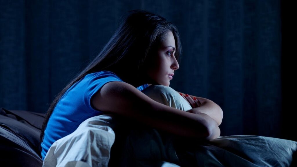 woman sitting on bed in dark with insomnia