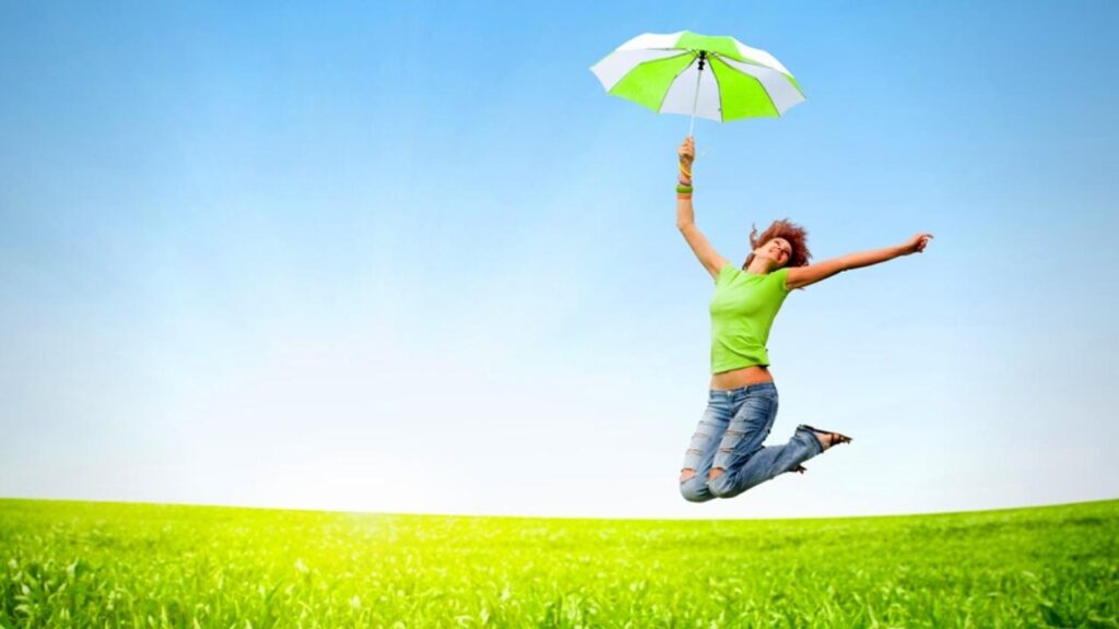 young woman jumping holding green umbrella over grass