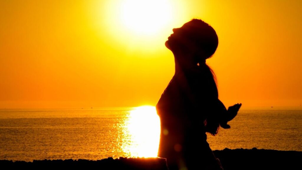 woman looking up with yellow sunrise background over sea