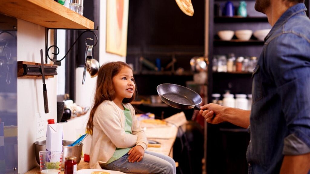little girl watching her father toss a pancake