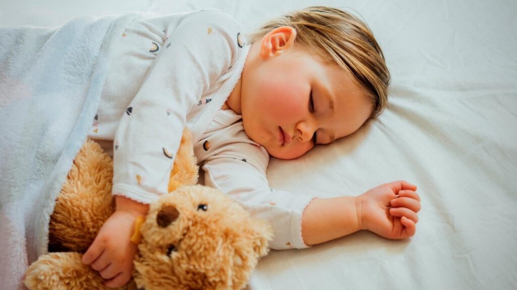young child asleep on bed holding onto teddy bear