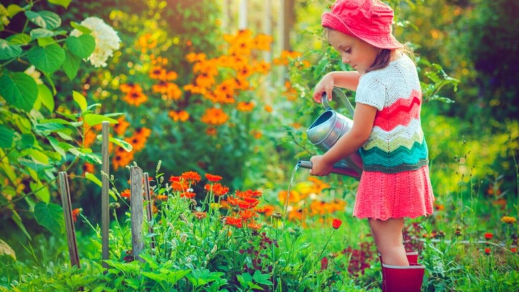 little girl in crocheted dress watering flowers in garden