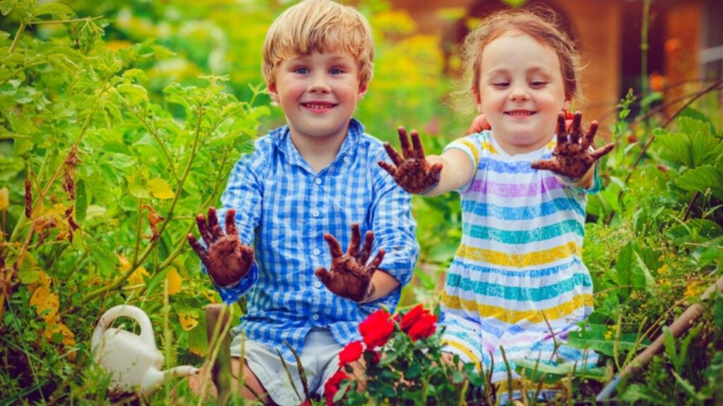 girl and boy sitting in garden holding up muddy hands