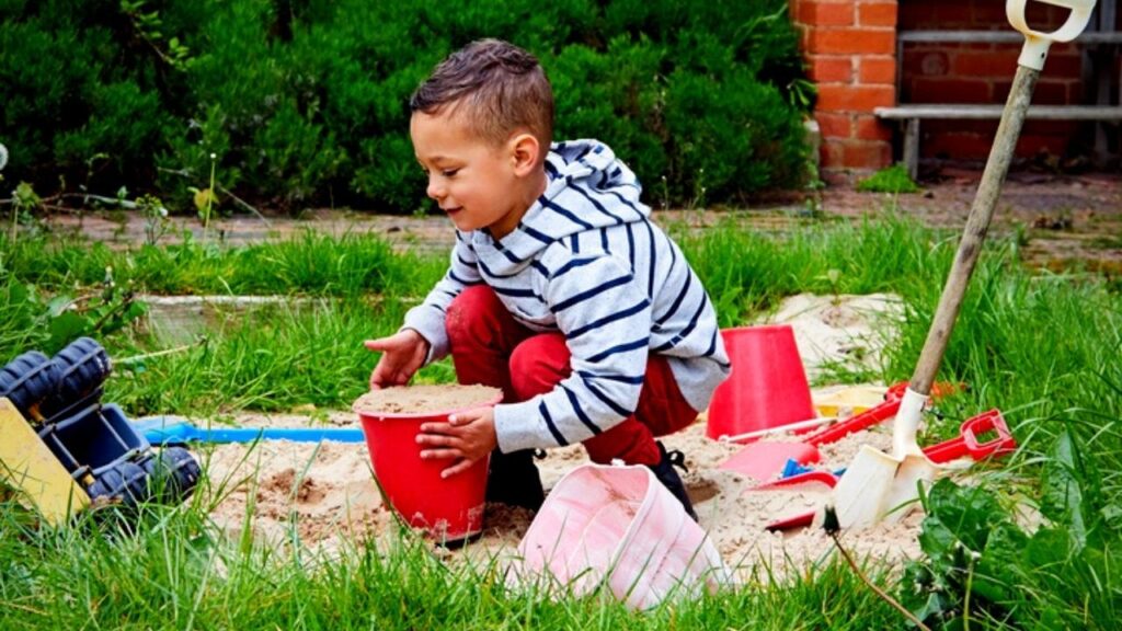 little boy playing in sand box in garden
