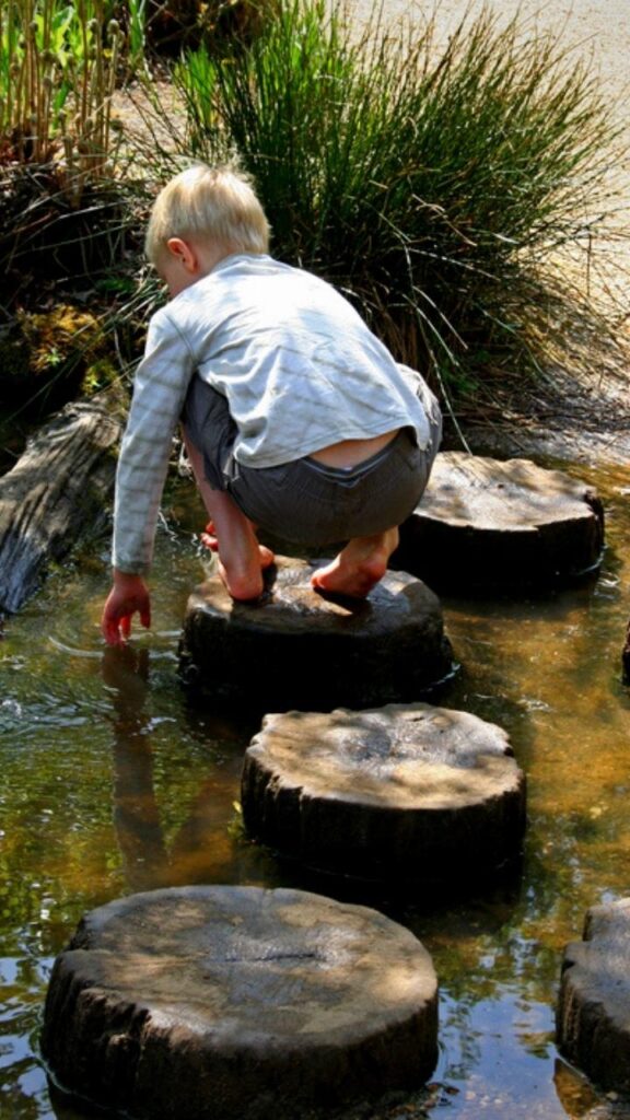 boy playing on stepping logs over water