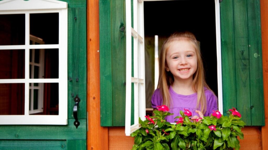 little girl looking out window of green playhouse