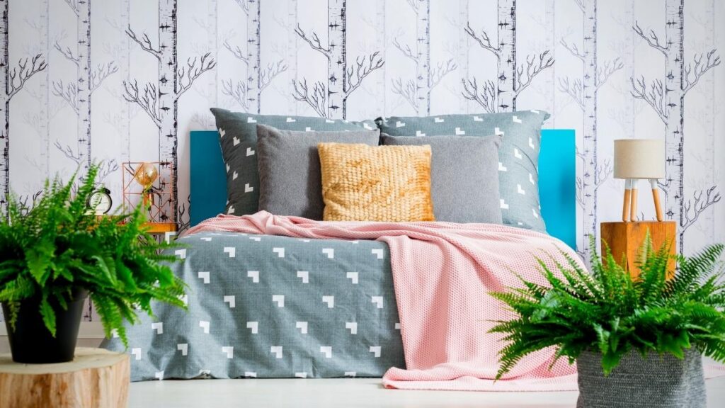 ferns and forest wallpaper behind bed with grey and pink throws