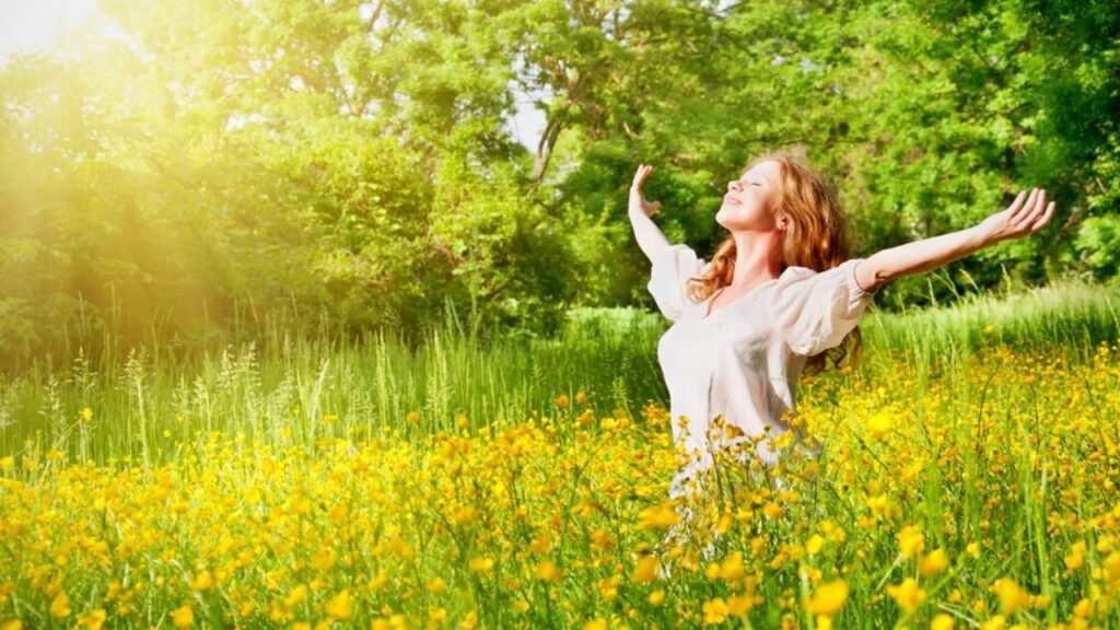 woman in sunny meadow stretching her arms to side