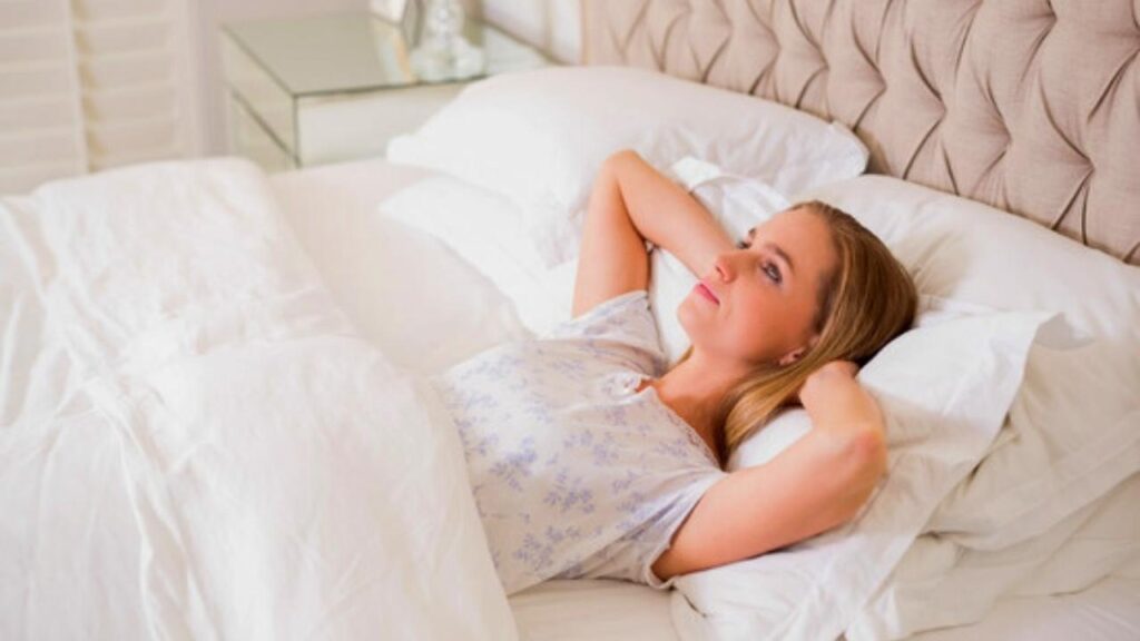 peaceful woman in bed with hands behind her head