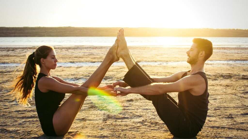 young couple stretching together on sandy beach