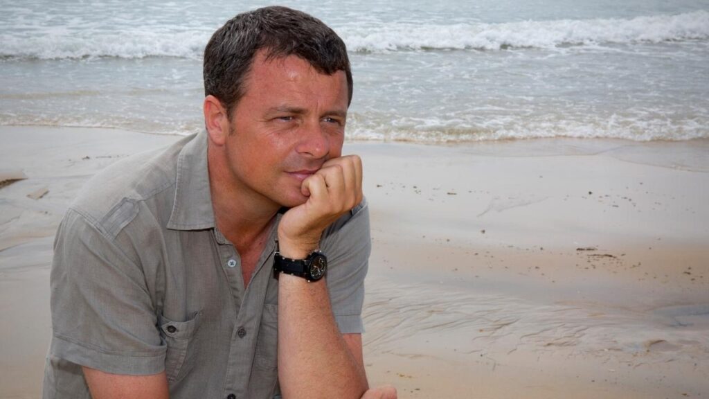 thoughtful man with healthy hair sitting on beach