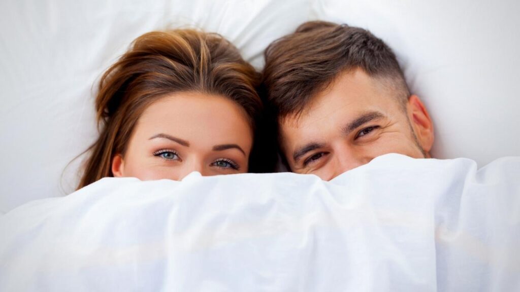 young couple peeping above white duvet 