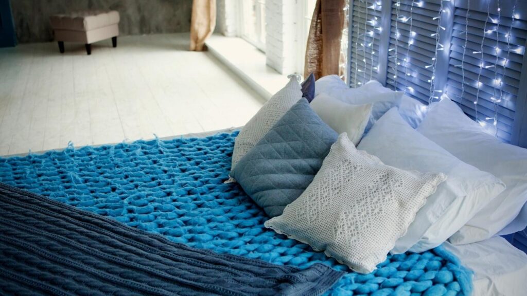 bed with blue knitted blanket and blue and white cushions