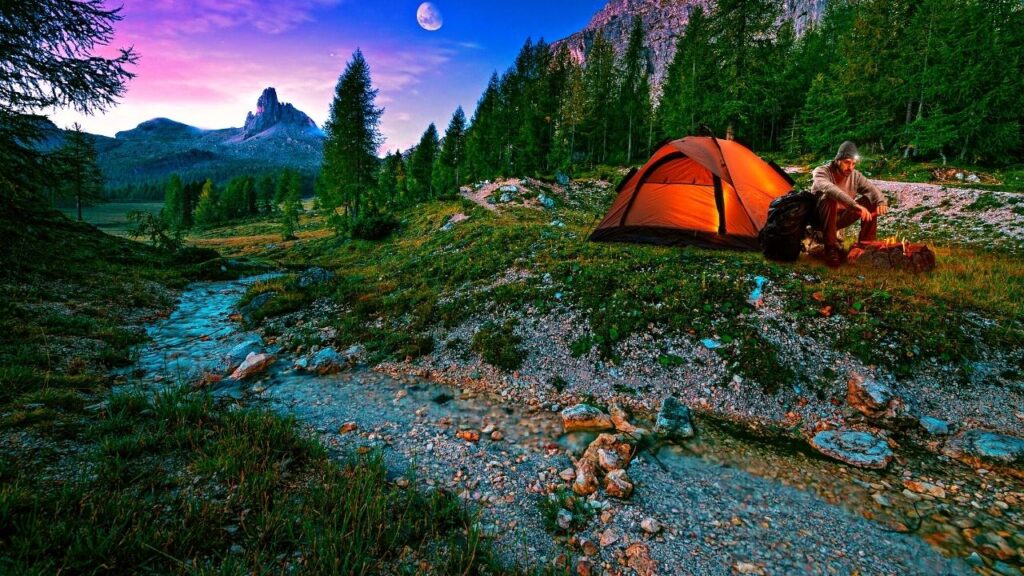 man beside campfire in hills