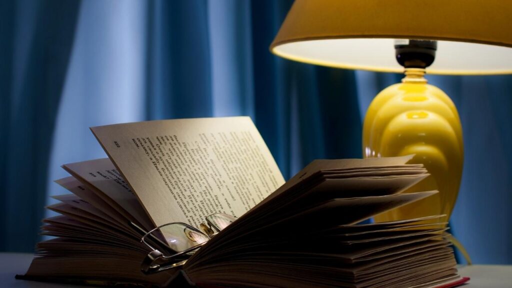 reading glasses on open book beside lamp