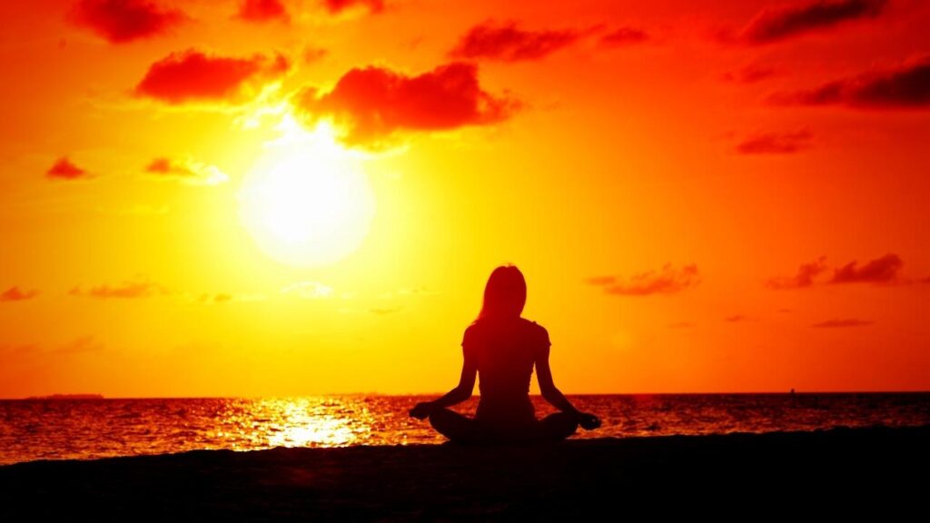 woman doing yoga on beach at sunset