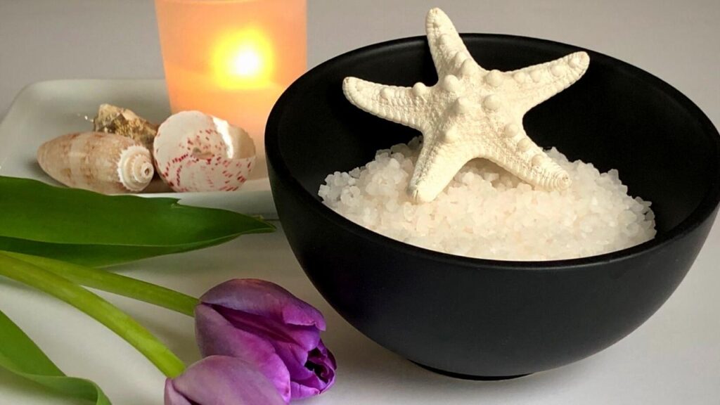 star fish in bowl of epsom salts beside lilac flowers and shells