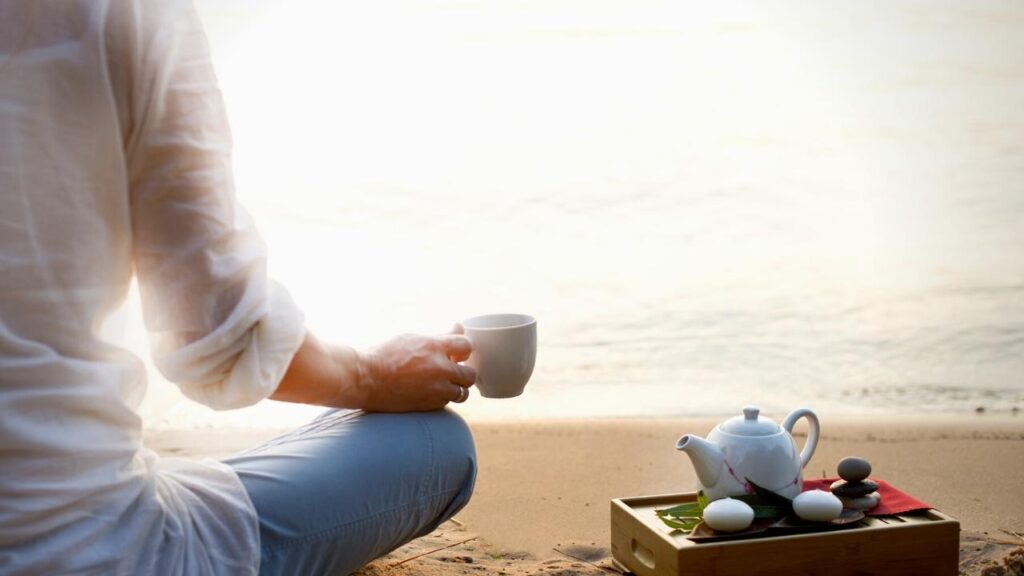 doing yoga on beach with cup of tea in hand