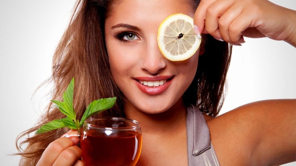 woman holding tea in hand and a slice of lemon over her eye