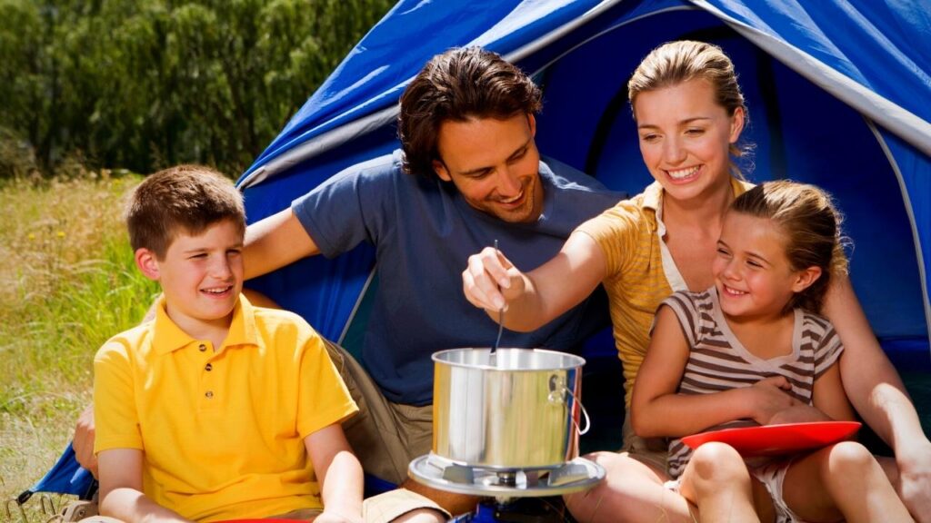 woman with family stirring pot outside tent