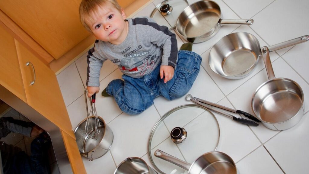 little boy sitting on floor among stainless steel pans