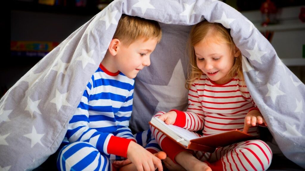 2 young children reading under the duvet
