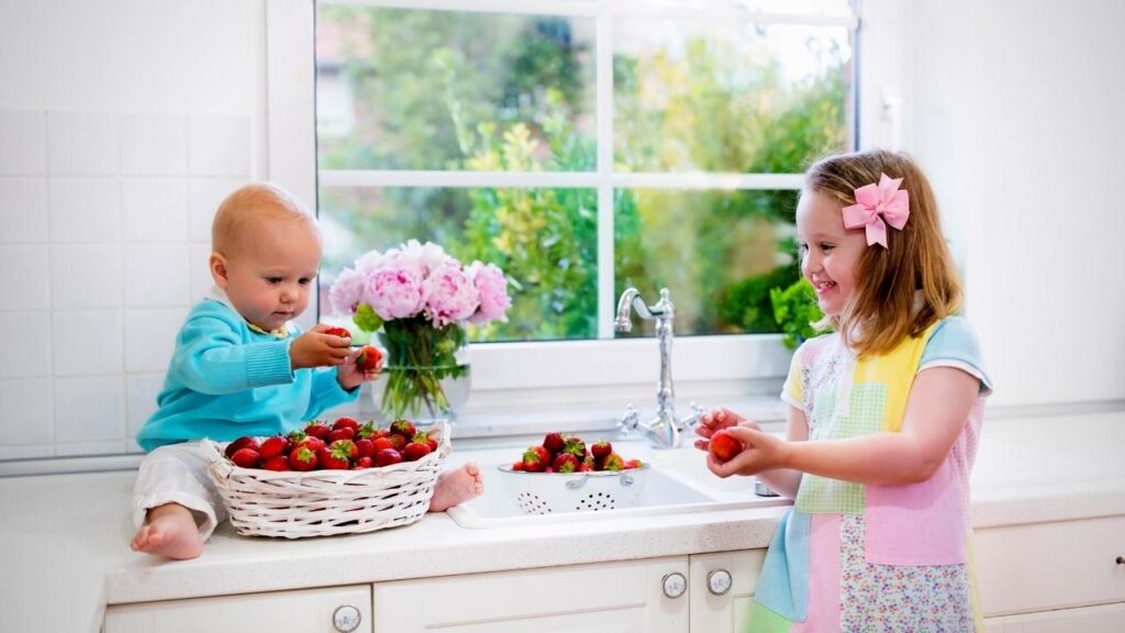 girl washing strawberries beside baby