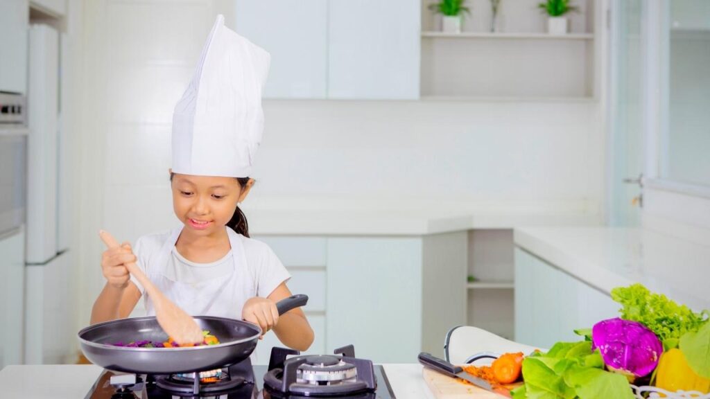 young girl with chefs hat cooking with pan