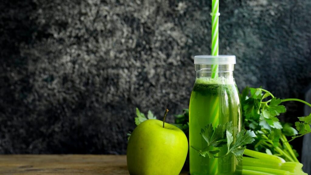 tall glass of green juice beside celery and apple